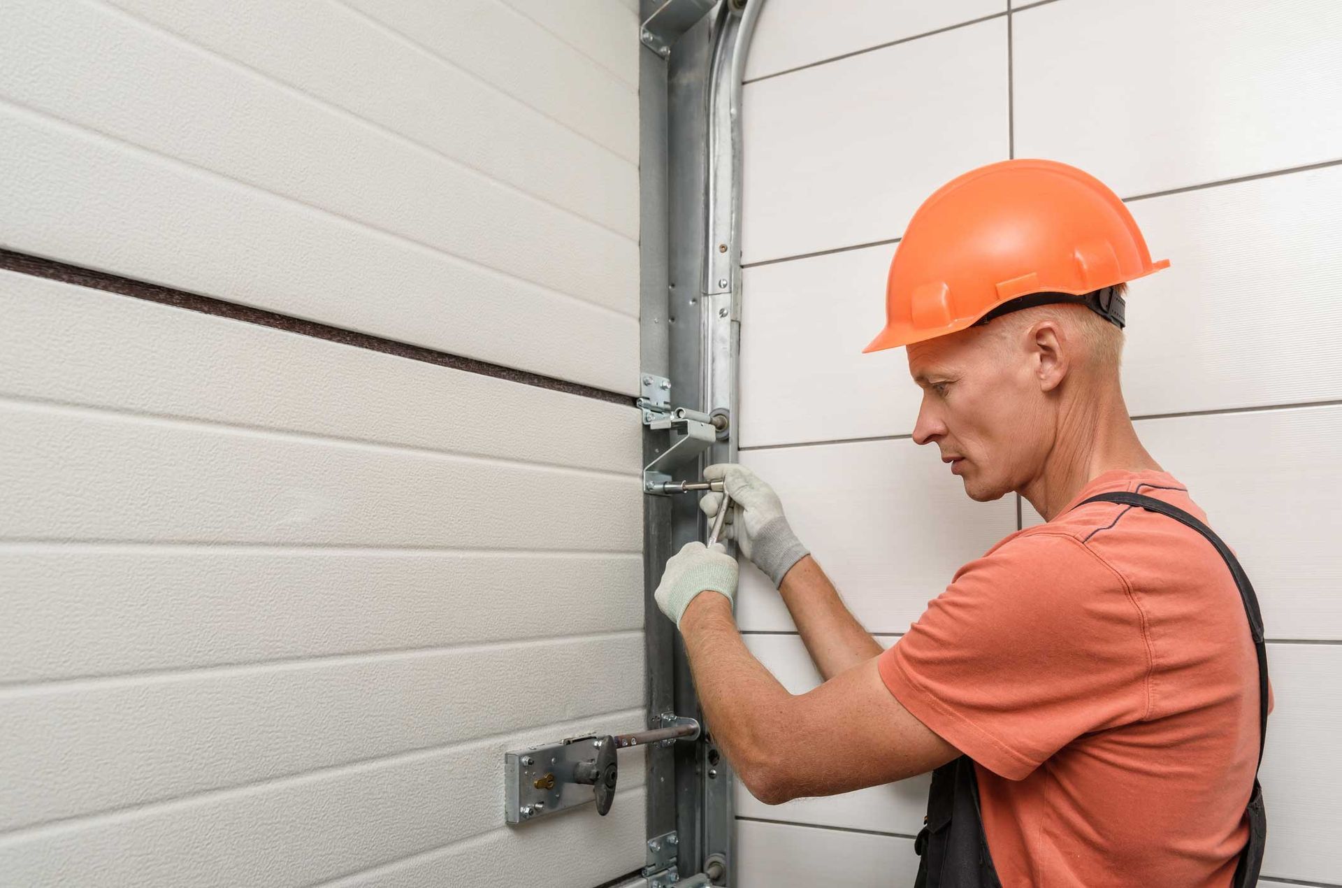 A man wearing a hard hat and gloves is working on a garage door.
