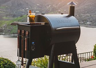 A smoker with grill utensils outside with a hillside in the background.