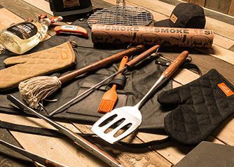 A selection of BBQ tools and accessories arranged on a wooden table.