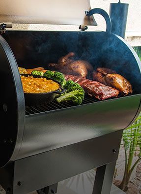 An outdoor grill with various foods cooking and smoke rising from it.