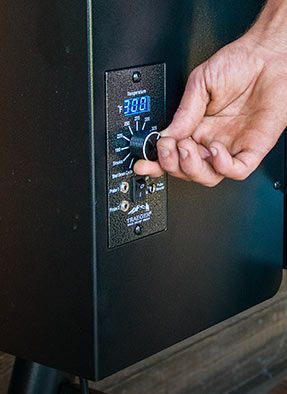 Image of someone's hand turning a dial on a grill to a specific temperature.