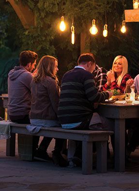 A diverse group of individuals sitting around a food table, engaged in conversation outdoors.