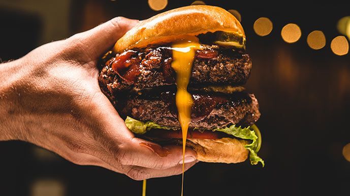  A person holding a massive double burger with melted cheese, lettuce and ketchup.