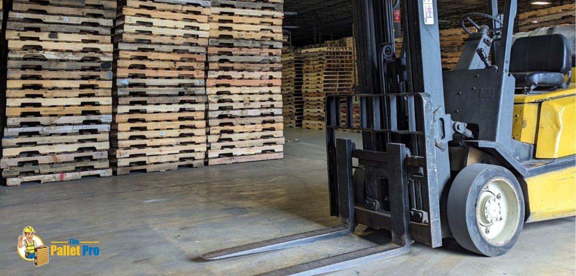 A forklift is driving through a warehouse filled with wooden pallets.