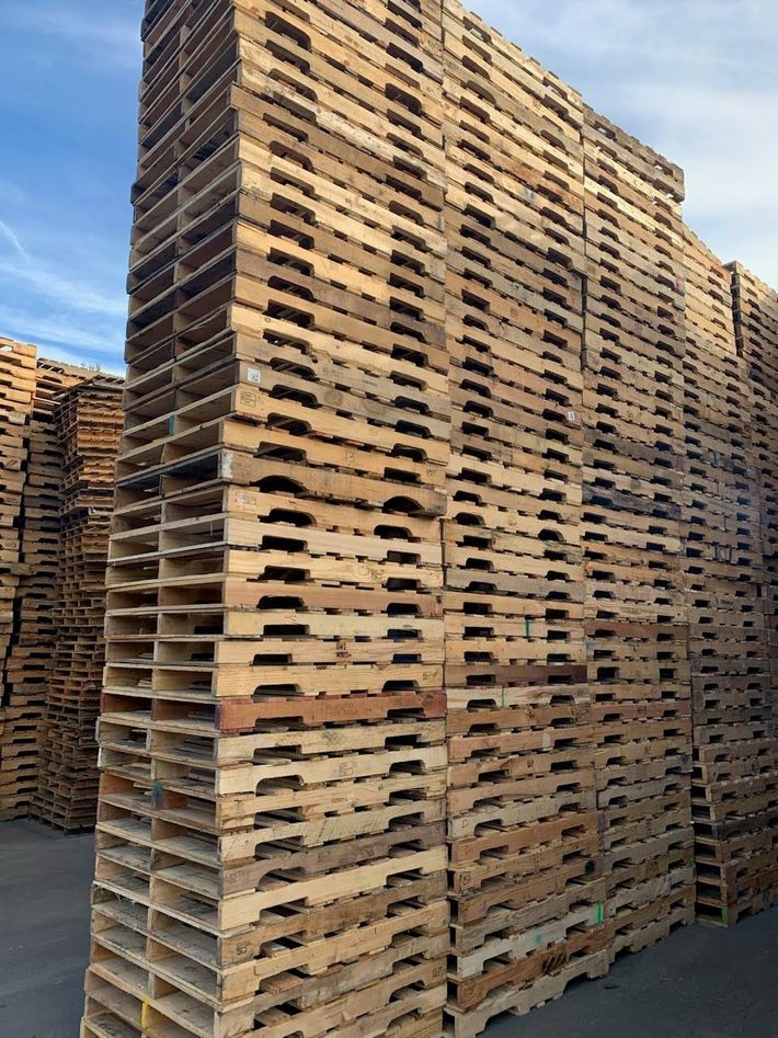 A pile of wooden pallets are stacked on top of each other in a parking lot.