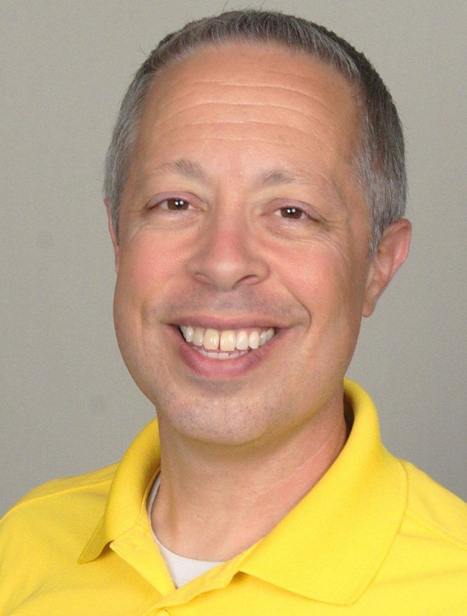 A man wearing a yellow shirt is smiling for the camera.