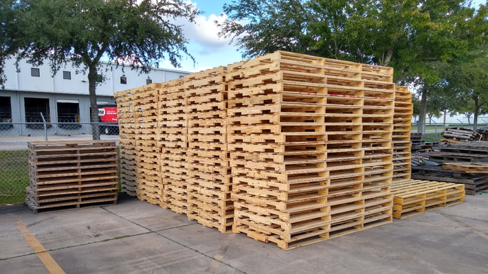 A pile of wooden pallets are stacked on top of each other in a parking lot.