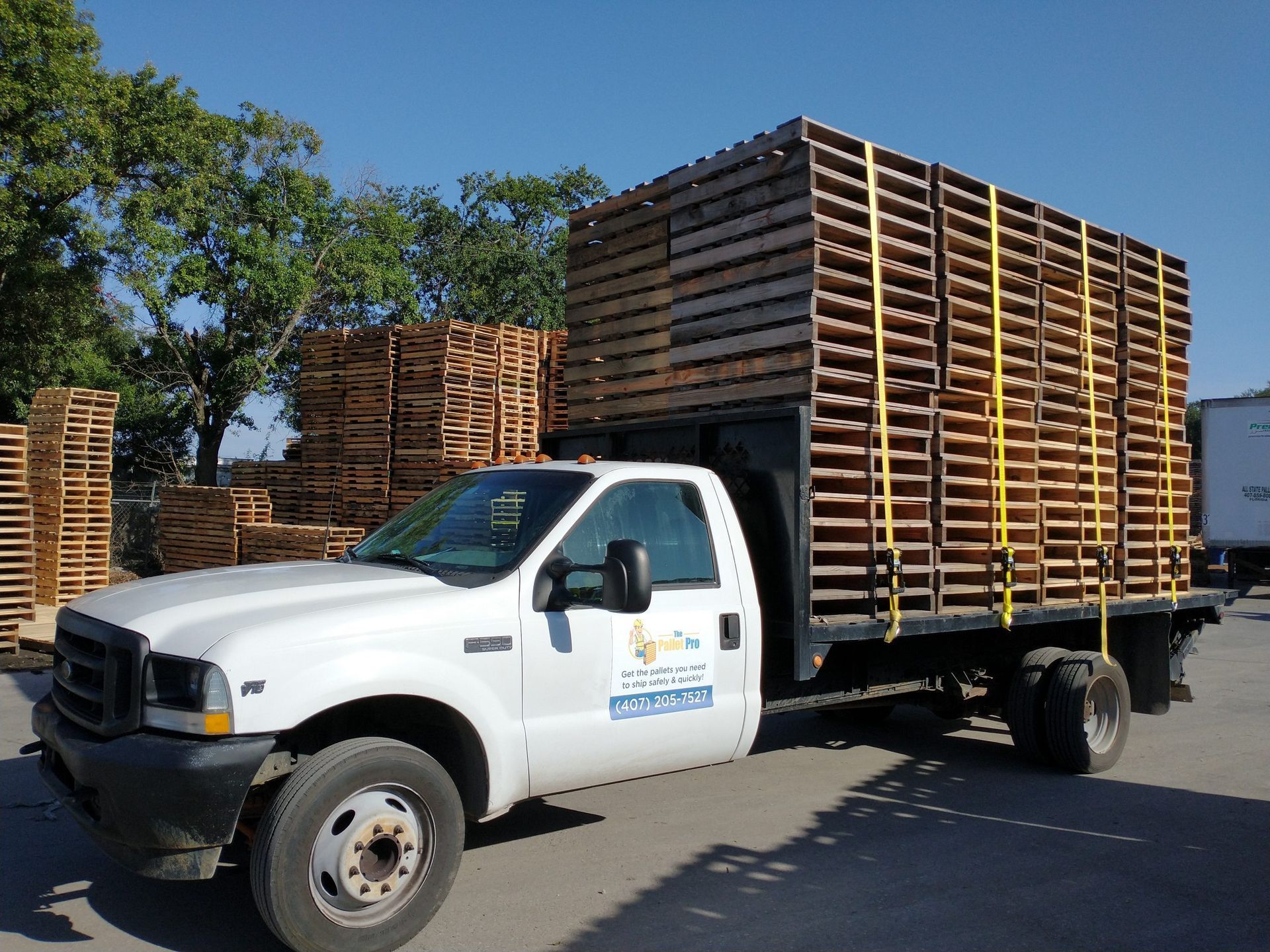 A white truck is parked in front of a pile of wooden pallets.