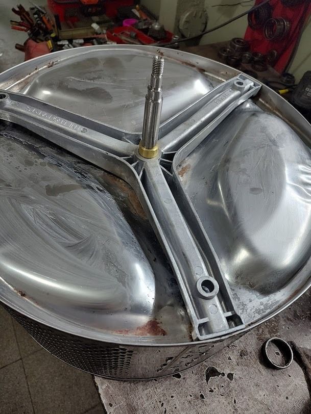 Tambor de lavadora con agitador de tres brazos. Componentes metálicos plateados, vista de cerca, contexto de reparación.