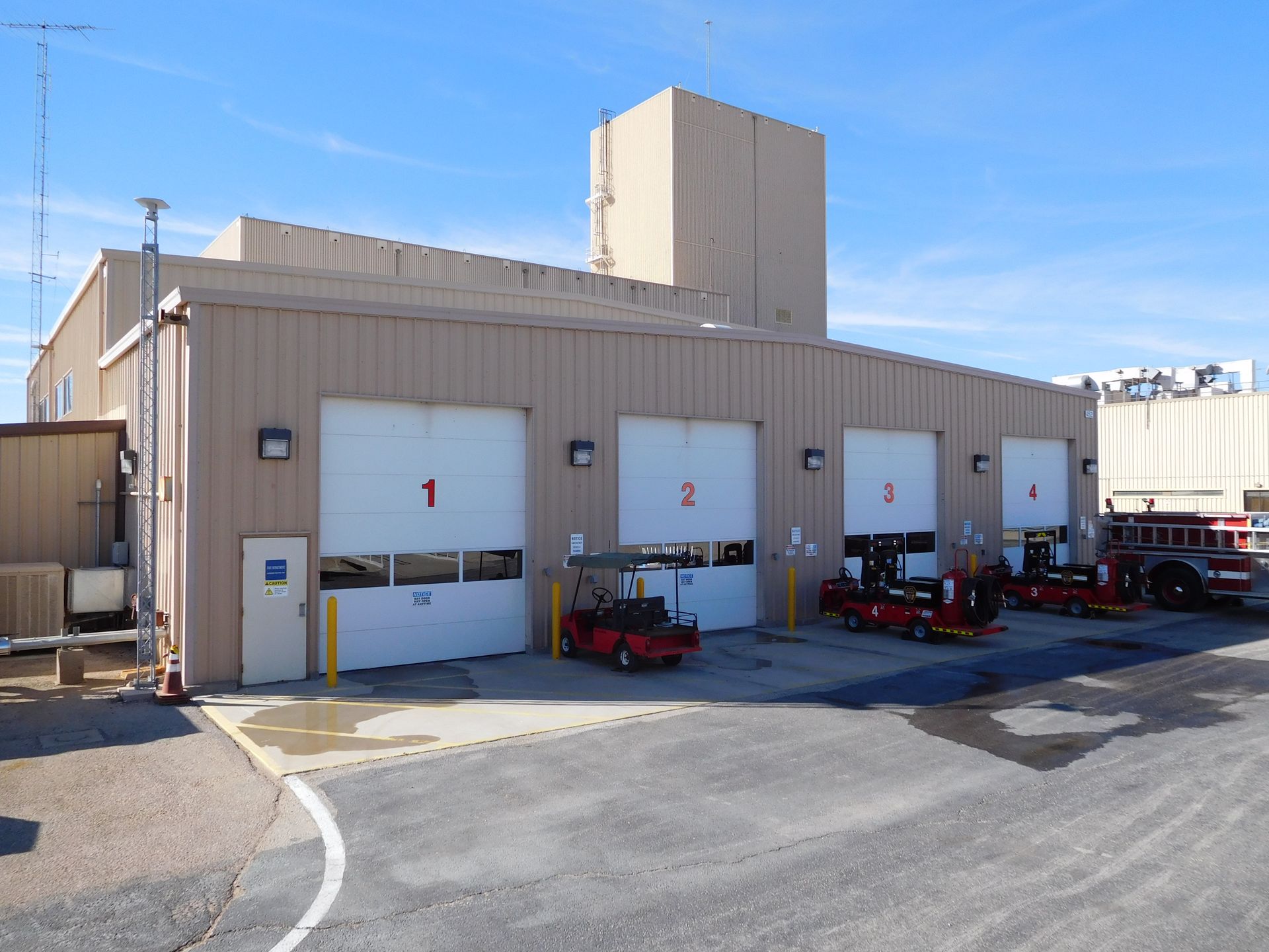 Garage with four bays, numbered doors, and vehicles parked inside. Beige building, blue sky.