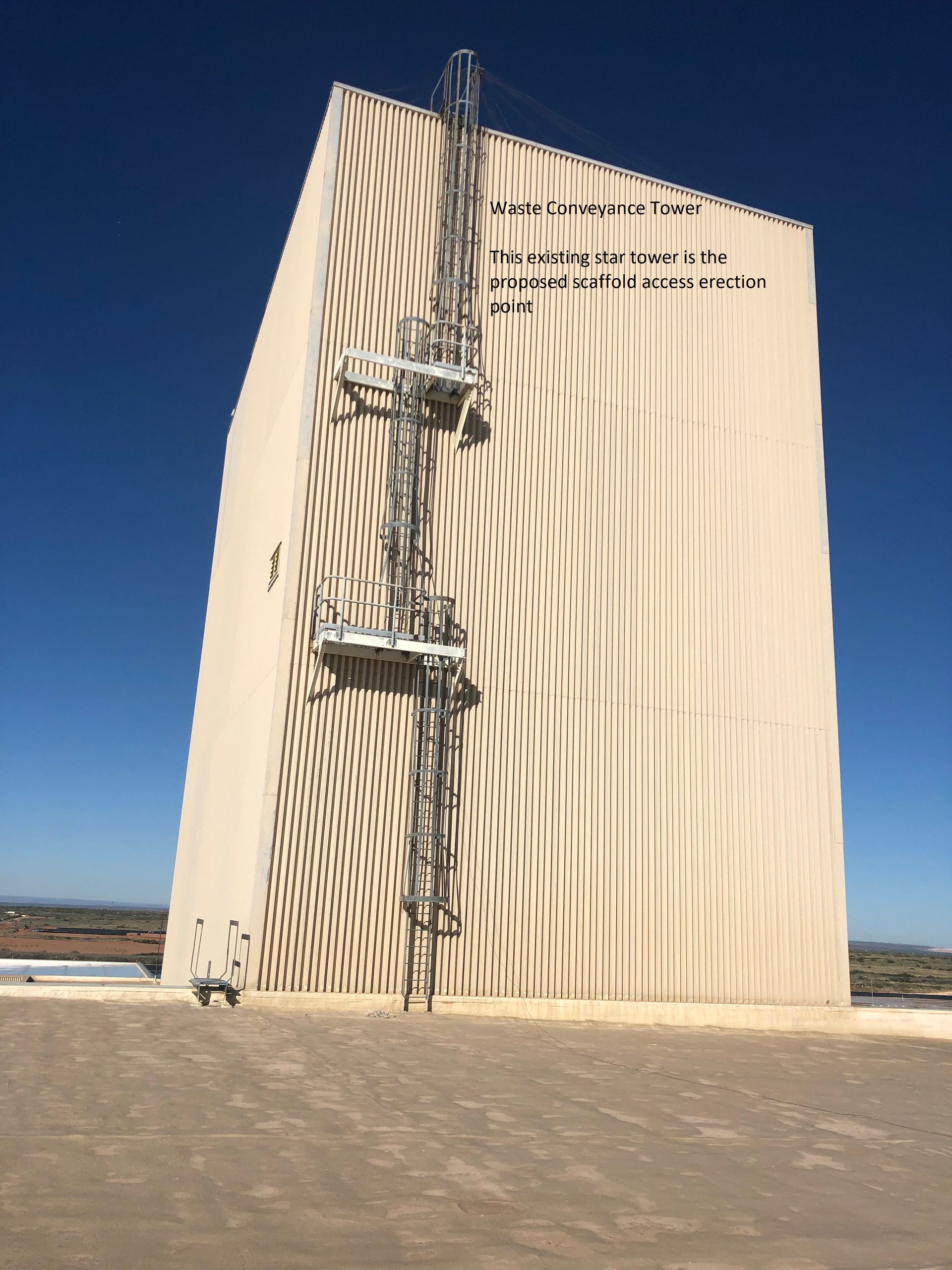 A tall, modern beige building with vertical lines and scaffolding on its side against a clear blue sky.