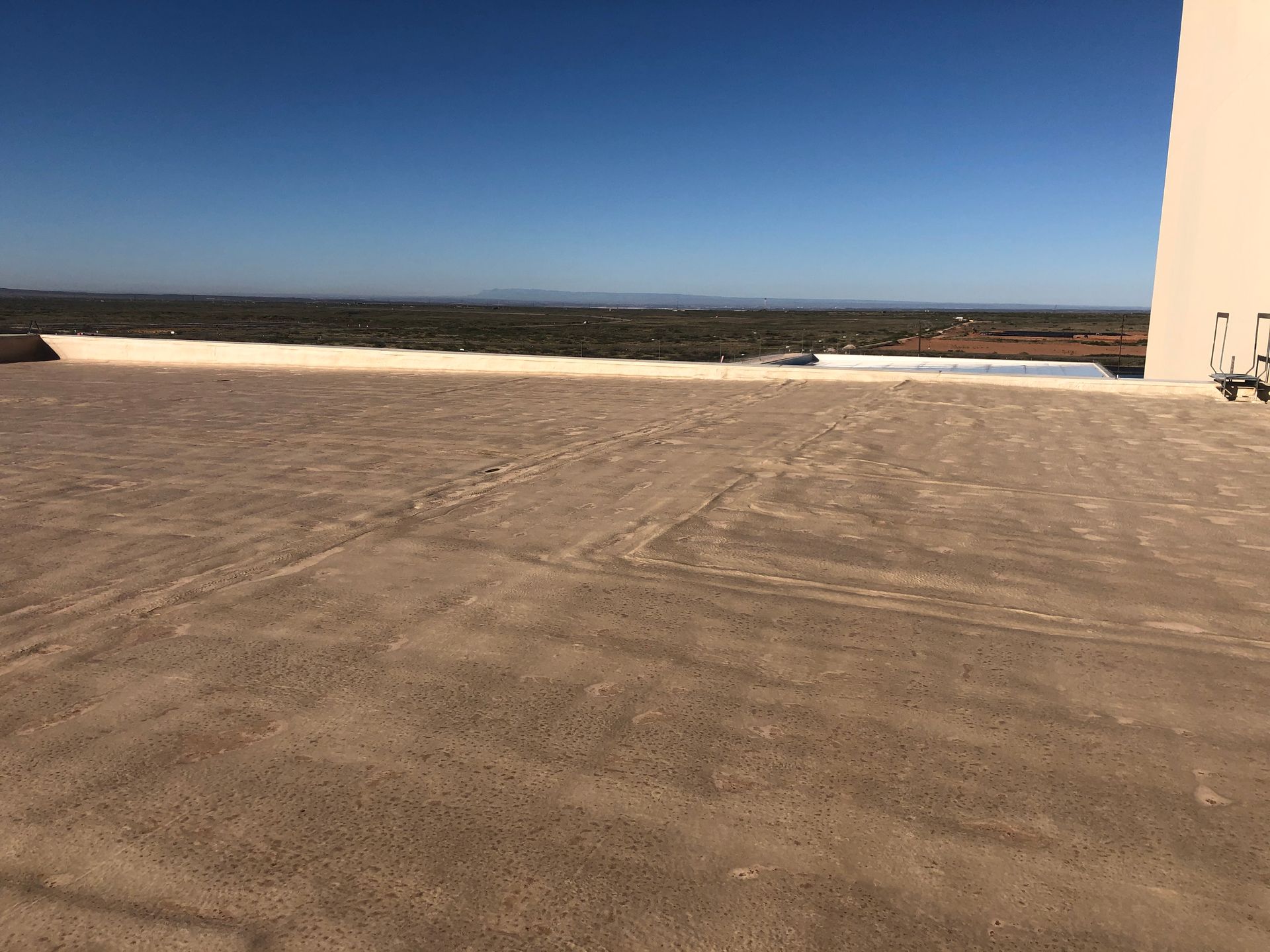 View from a rooftop: brown ground, blue sky, distant landscape with green, beige, and light brown.