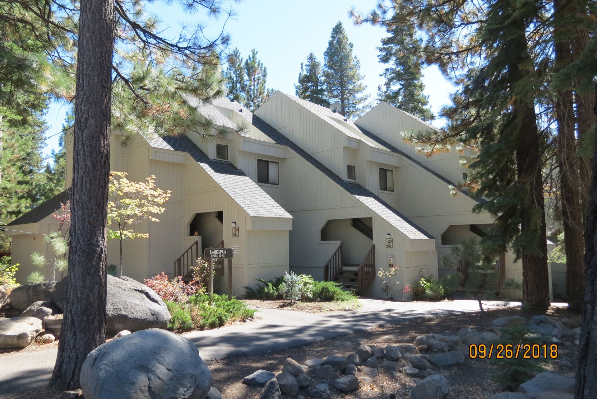 Beige multi-unit residential building with angled roofs, surrounded by trees.