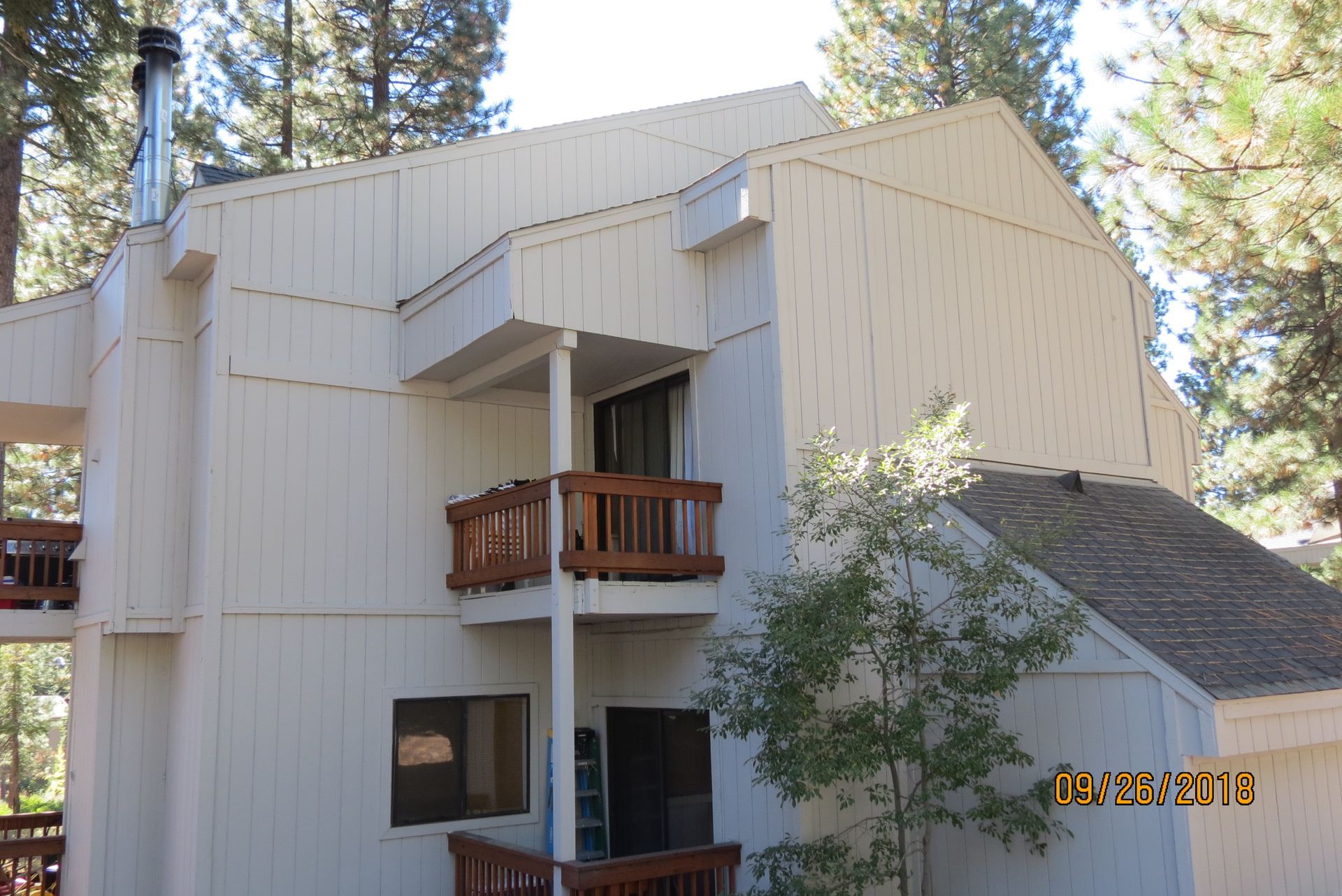 Beige two-story building with wood balconies, set in a wooded area.