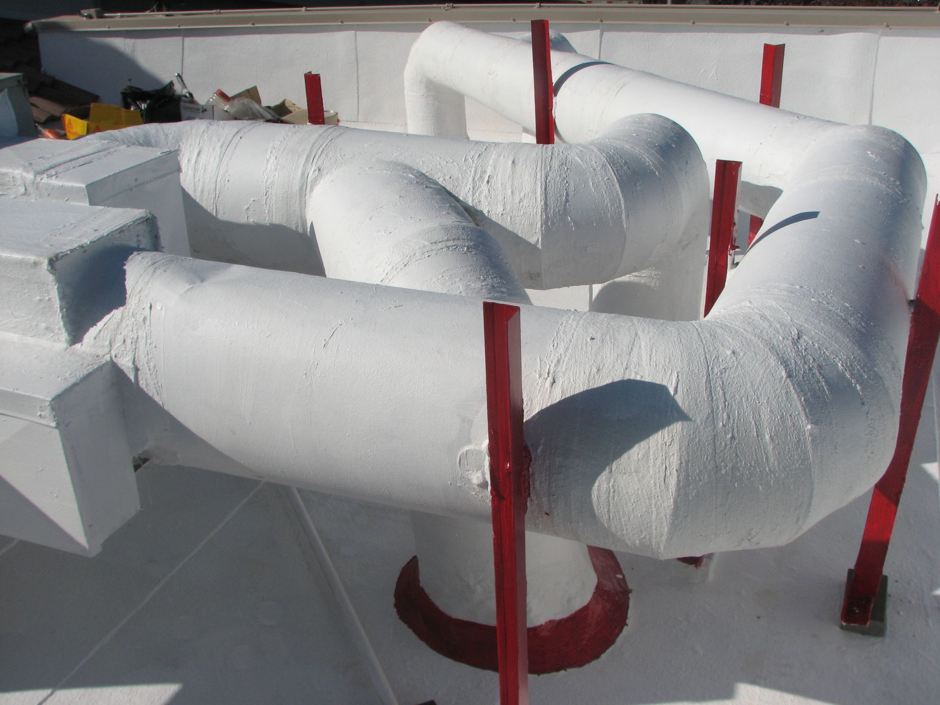 White insulated pipes with red supports on a flat, white surface.