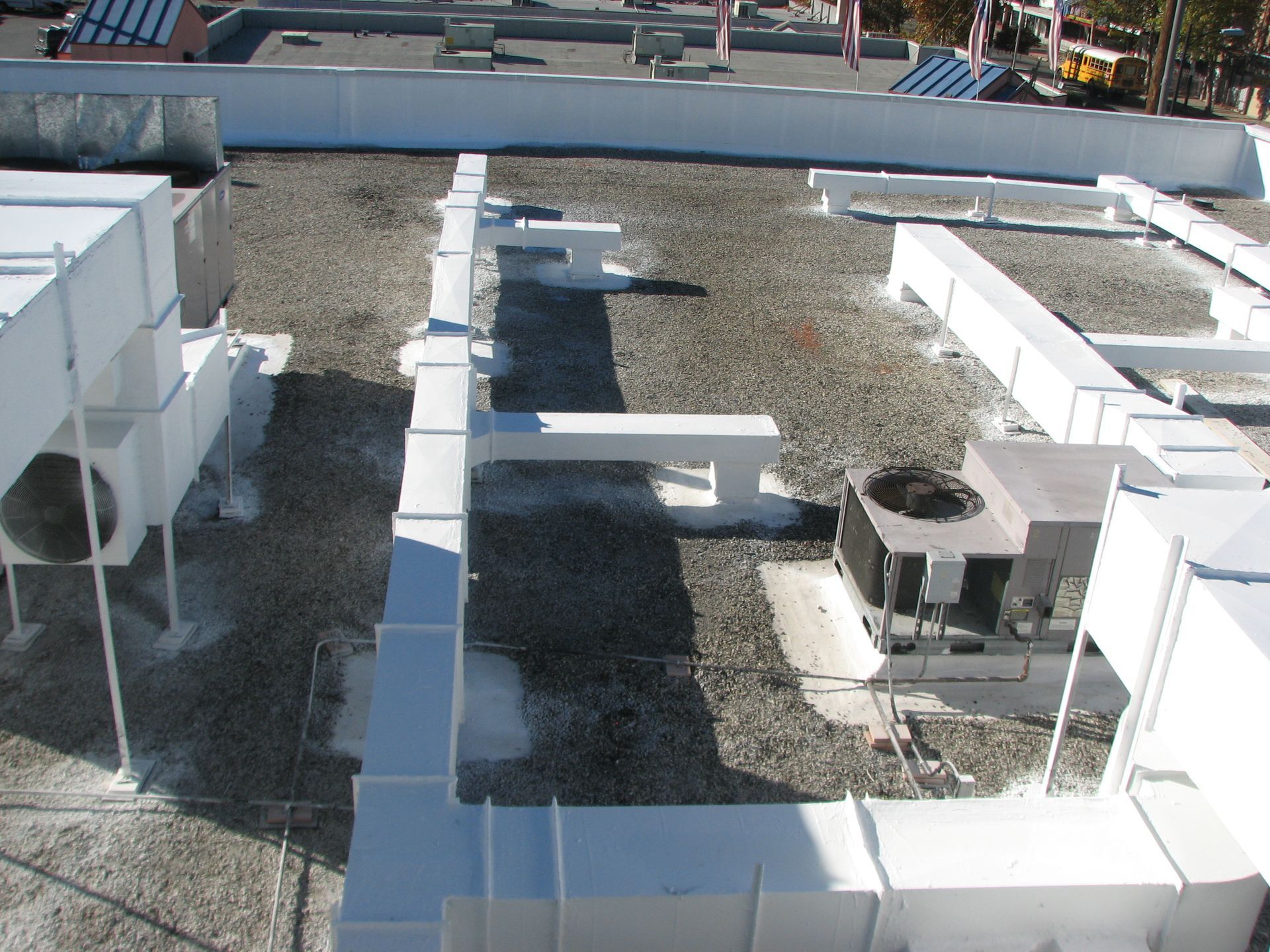 White HVAC ducts and units on a gravel-covered rooftop under a bright sky.