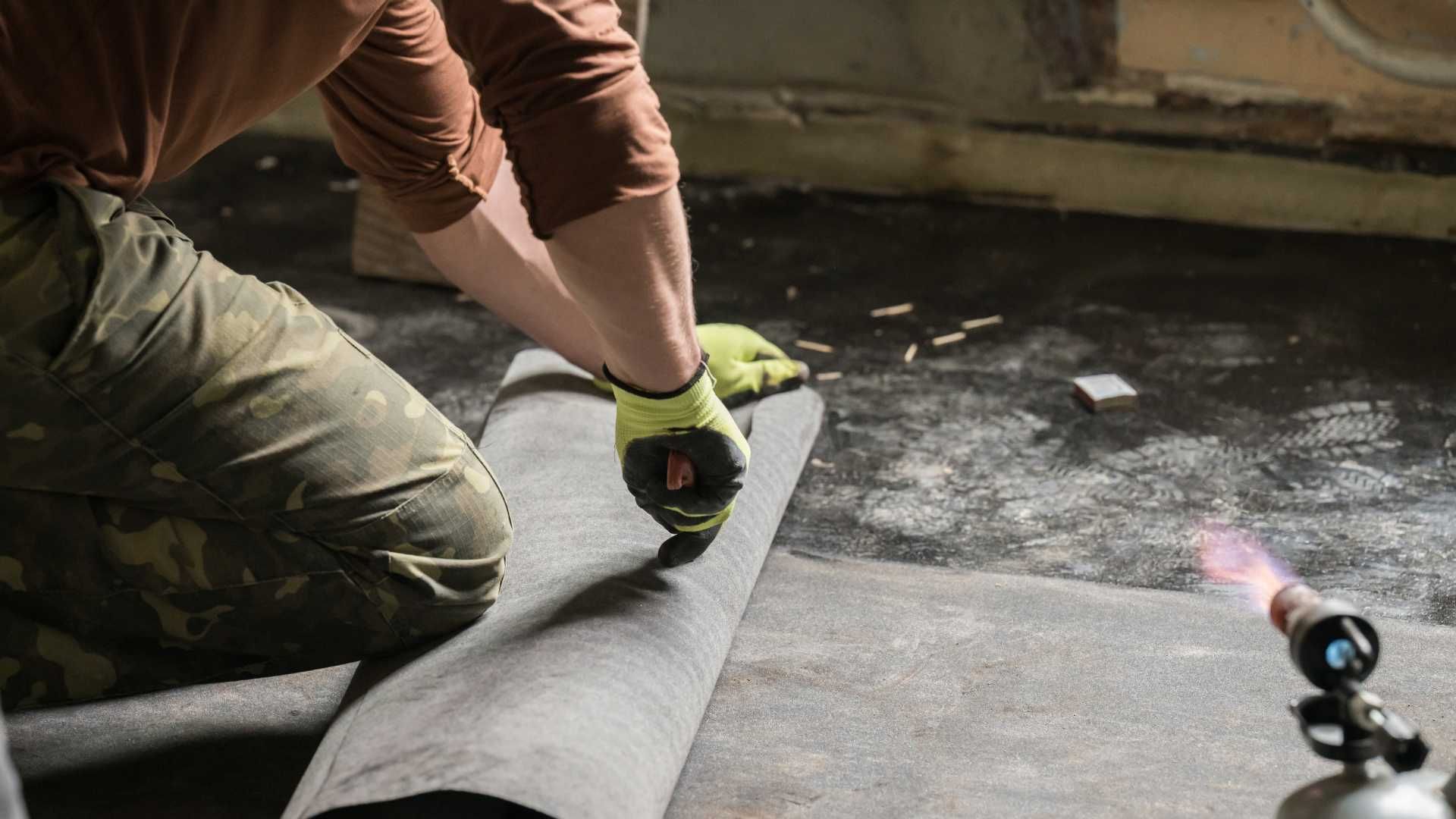 A man is kneeling down and cutting a piece of carpet with a torch.
