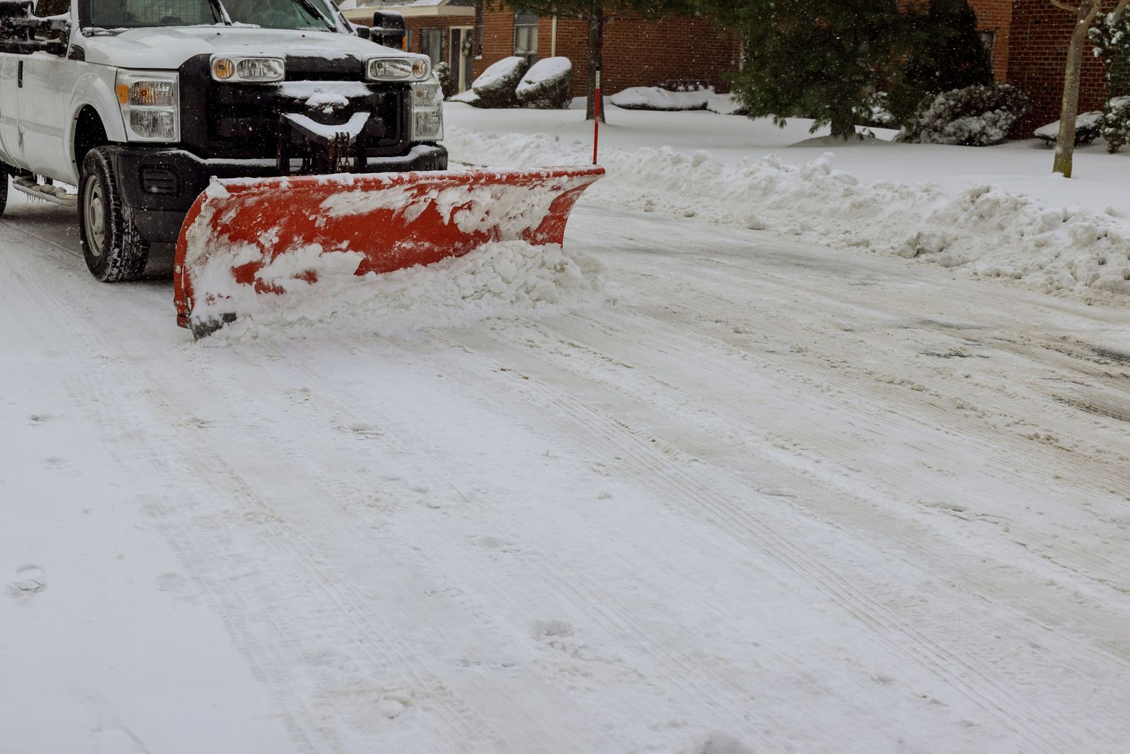 A white truck is plowing snow on a snowy street.
