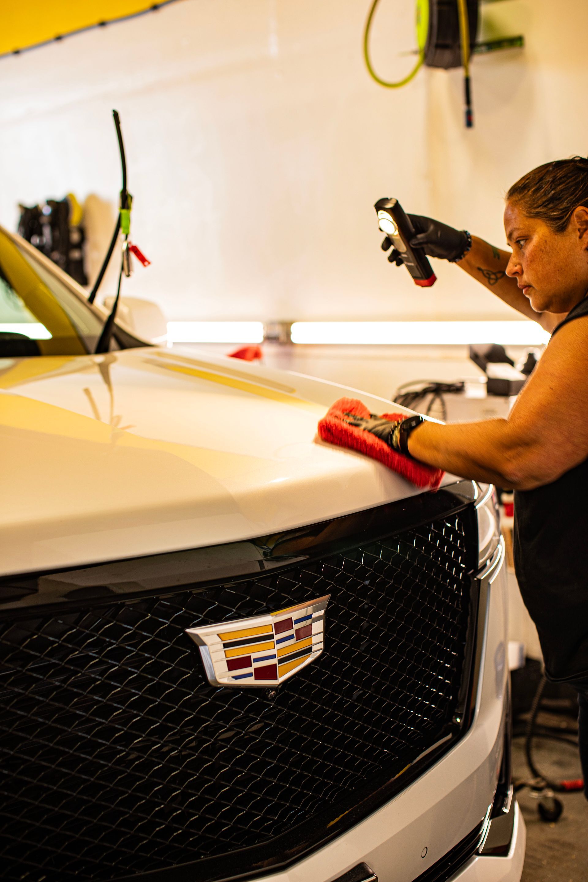 A woman is cleaning the hood of a white cadillac in a garage.