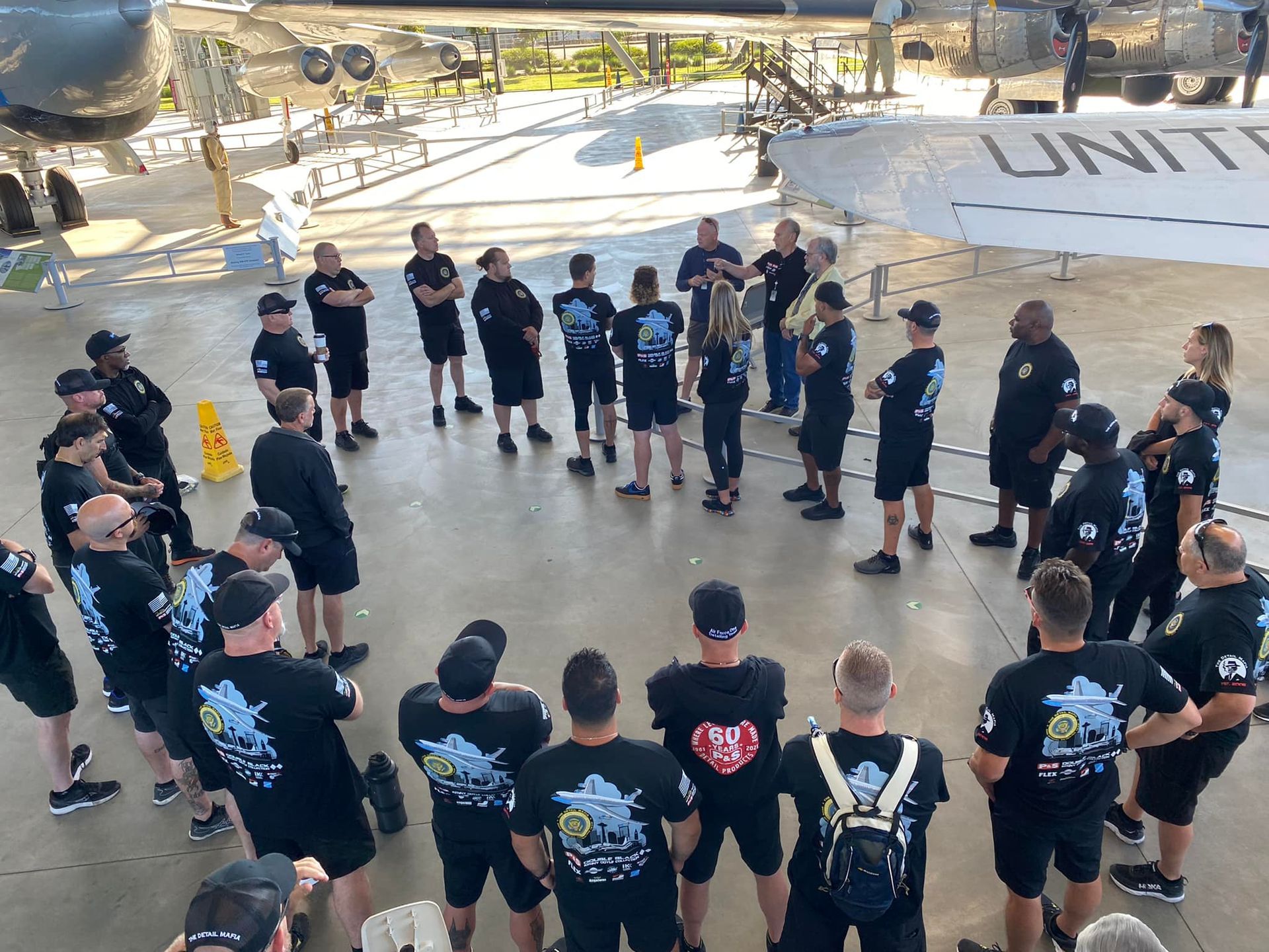 A group of men are standing in a circle in front of an airplane.