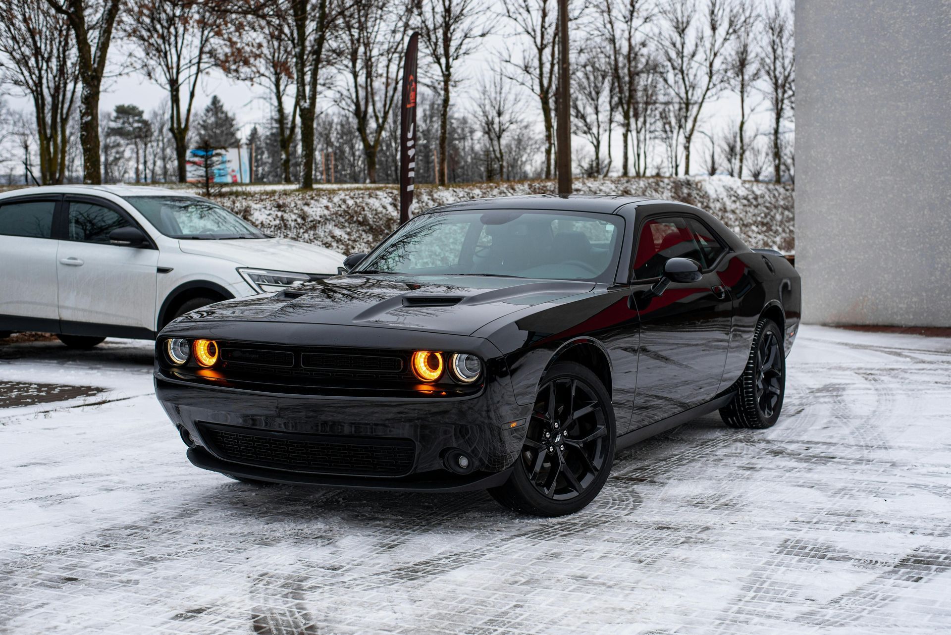 A black dodge challenger is parked in the snow.