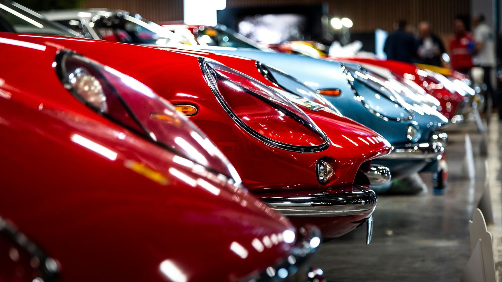 A row of red and blue cars are parked next to each other in a garage.