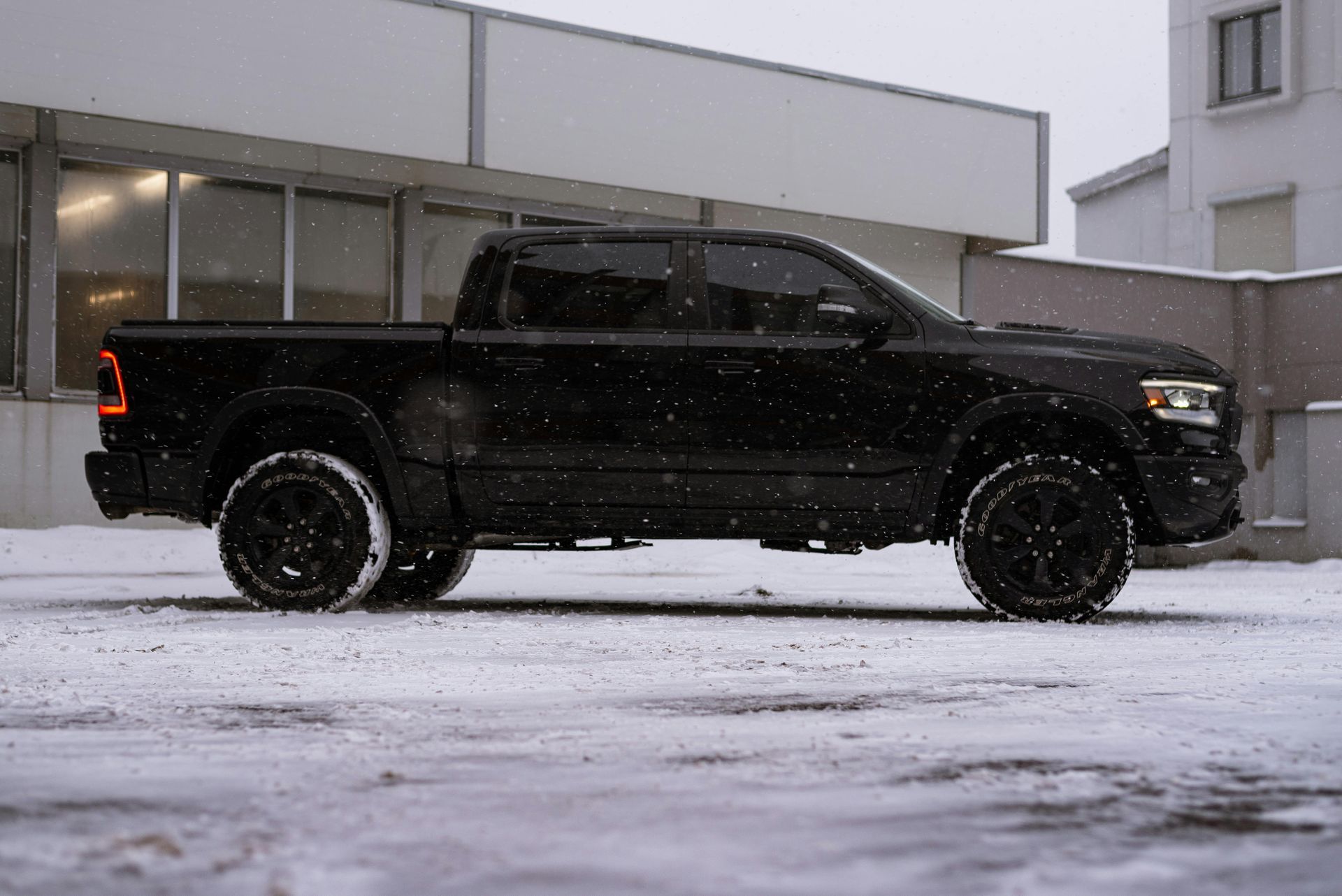 A black truck is parked in the snow in front of a building.