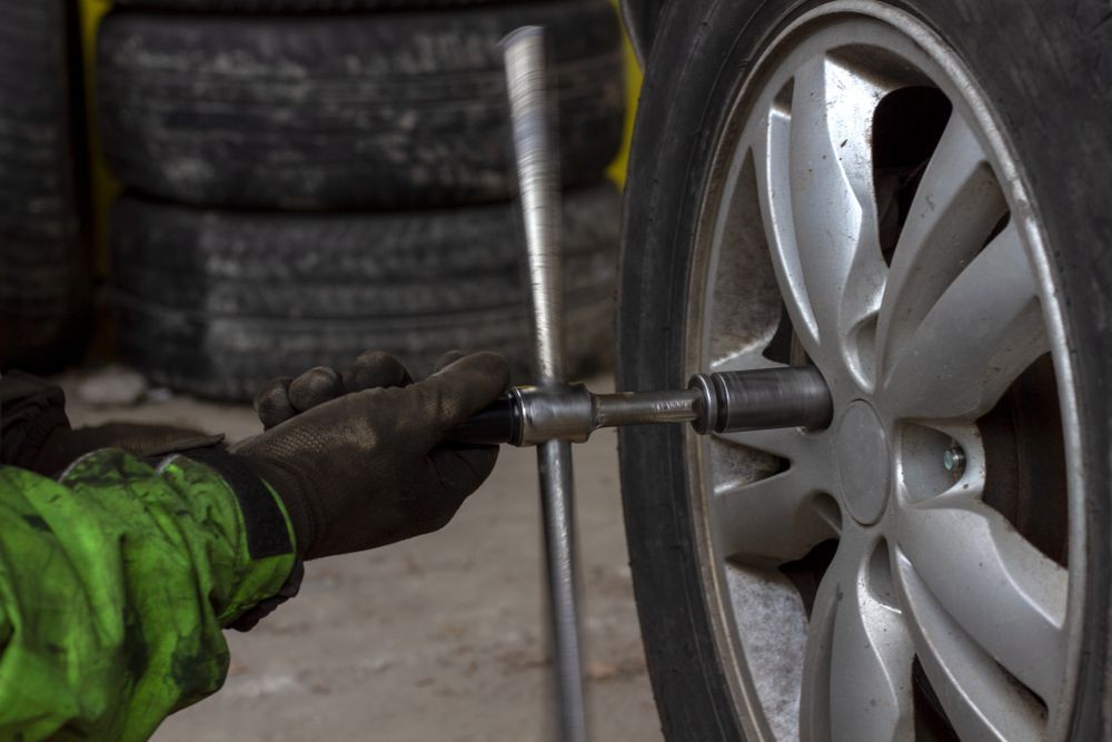 A Mechanic In A Green Jacket Uses A Socket Wrench To Tighten — THG Tires in Gladstone Central, QLD