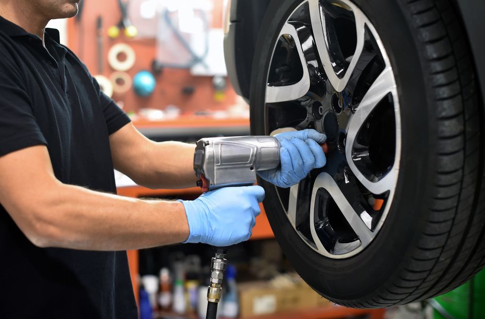 A Mechanic Wearing Blue Gloves Uses A Pneumatic Impact Wrench — THG Tires in Gladstone Central, QLD