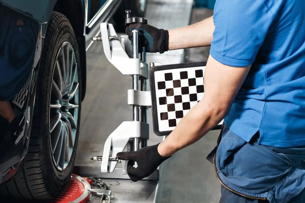 A Technician In A Blue Uniform Attaches A Wheel Alignment Sensor — THG Tires in Gladstone Central, QLD