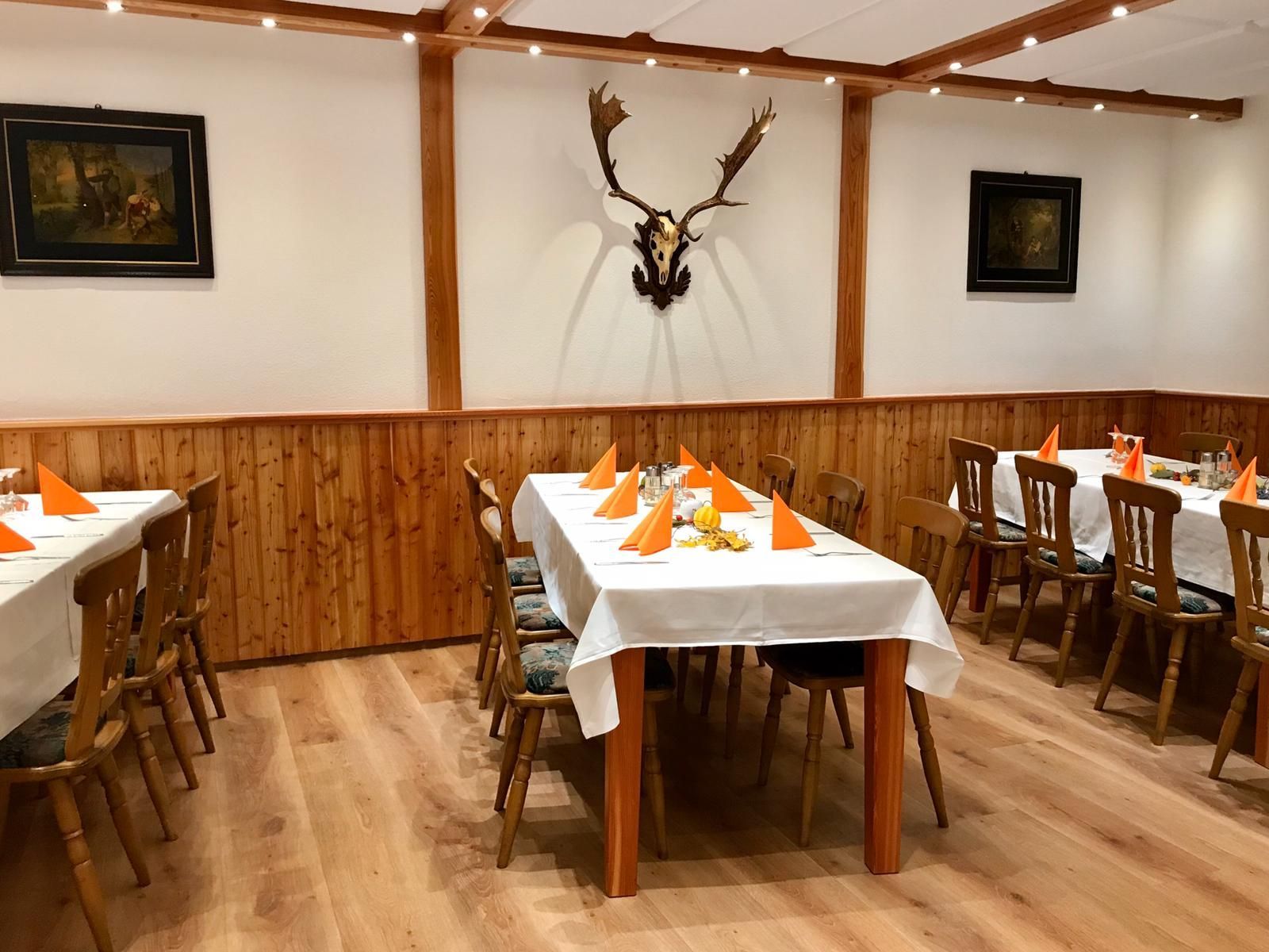 Esszimmer mit Holzvertäfelung, mit weißen Tischdecken und orangefarbenen Servietten gedeckte Tische, geschmückt mit Tierschädeln.