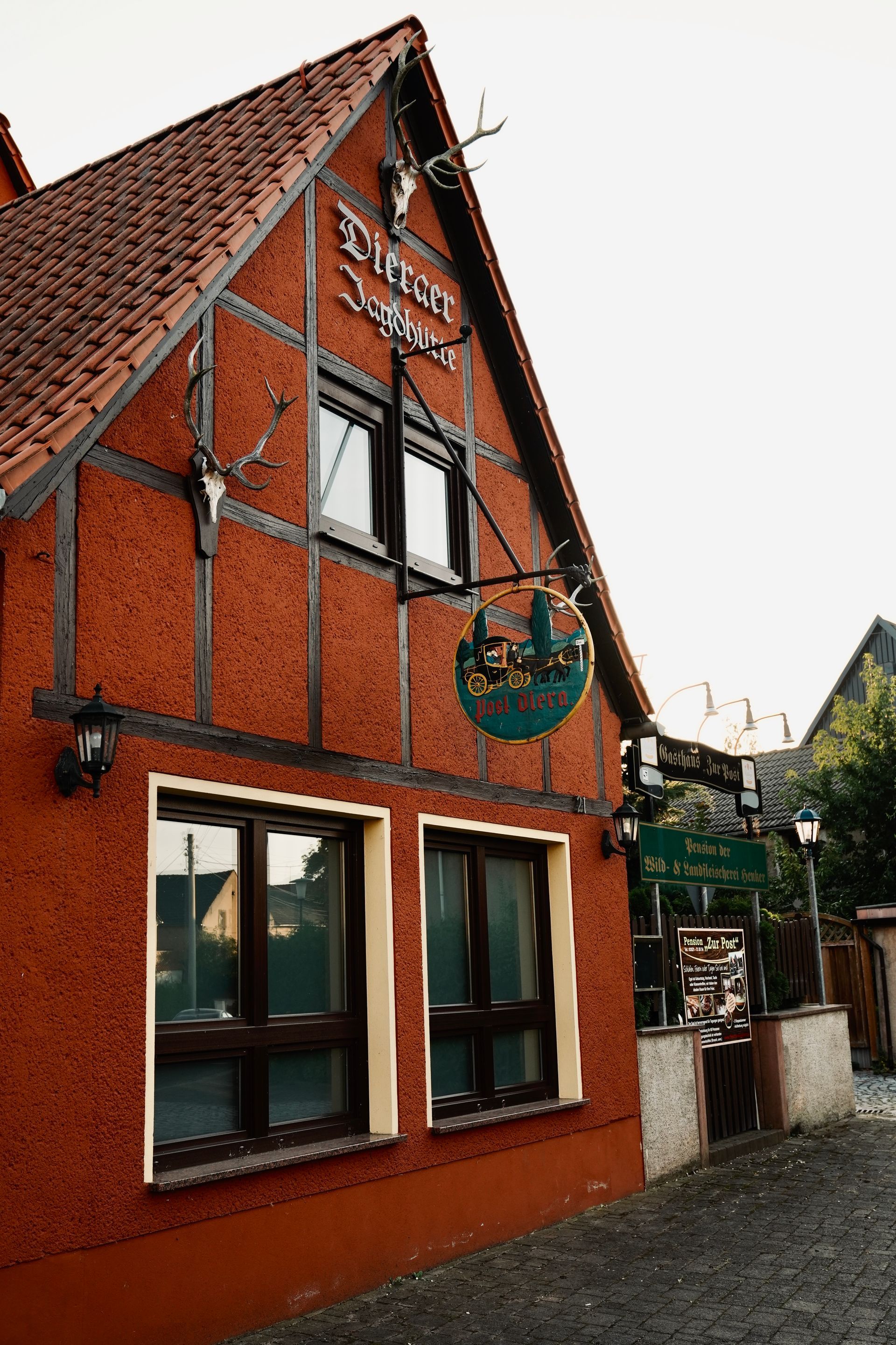 Rotes Gebäude mit braunen Fachwerkakzenten, einem Schild mit der Aufschrift „Restaurant Jäger“ und dekorativen Hirschgeweihen.
