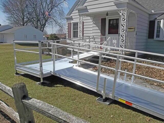 White wheelchair ramp with railings leading to a house entrance on a sunny day