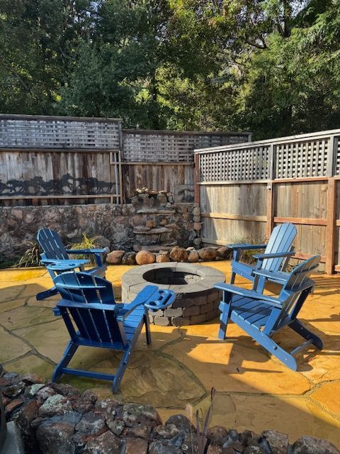Blue chairs around a fire pit on a concrete patio, wooden fence in background.