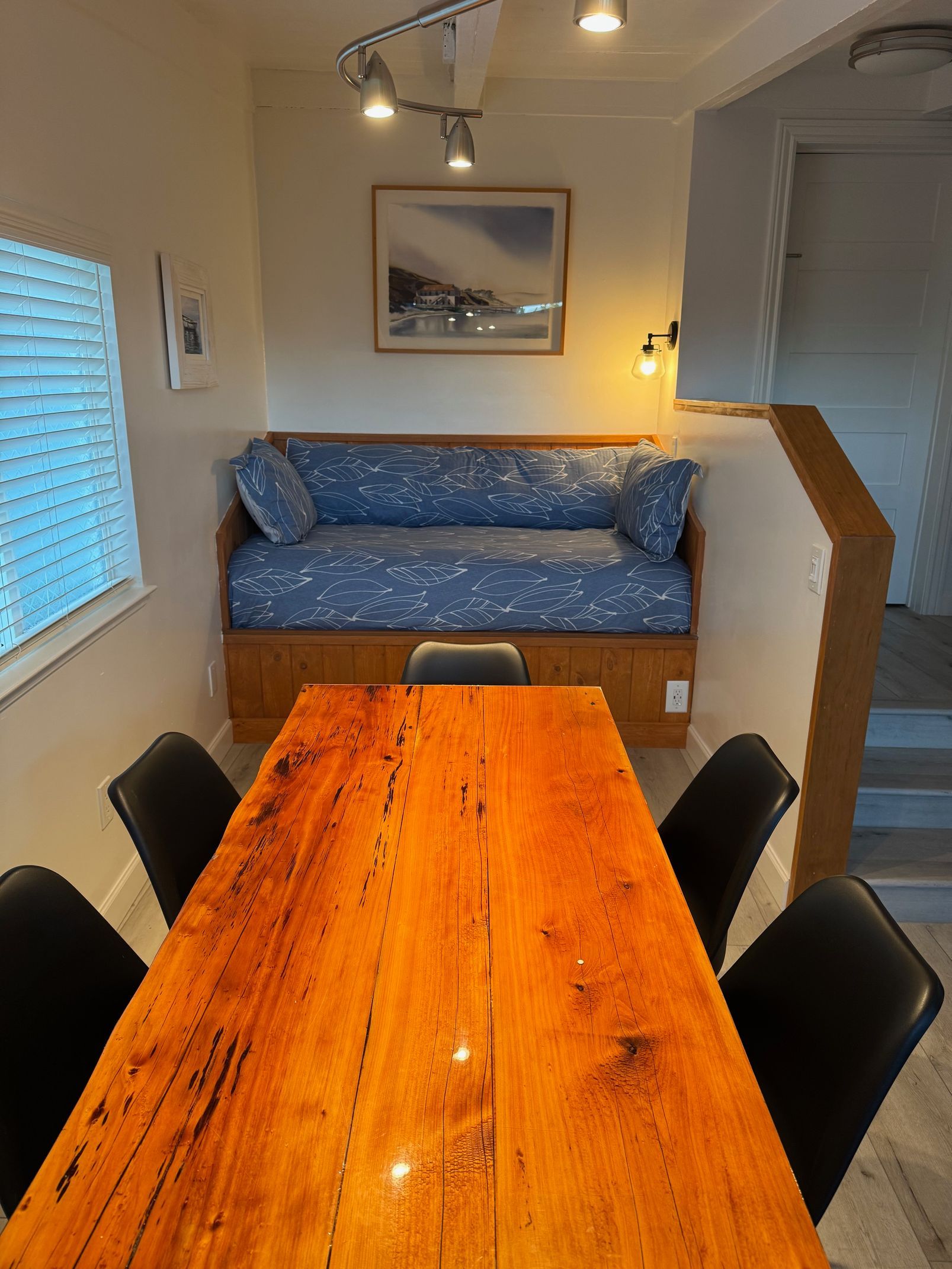 Dining room with wooden table and chairs, built-in sofa, window, artwork, and staircase.