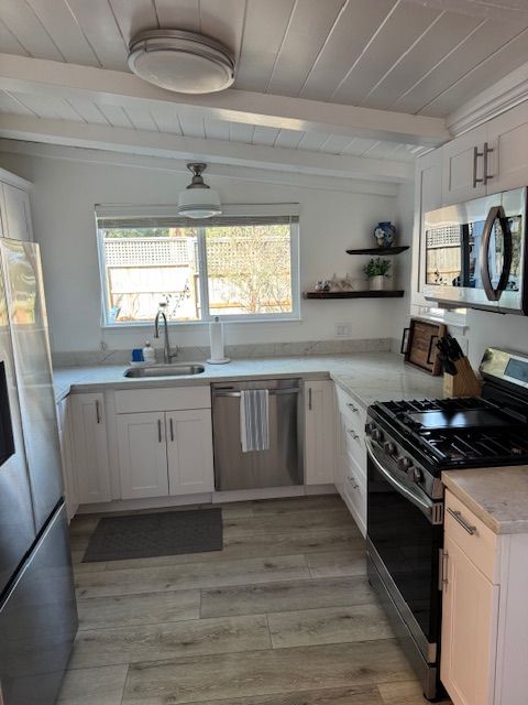 White kitchen with stainless steel appliances, light countertops, wood-look floor, and a window.