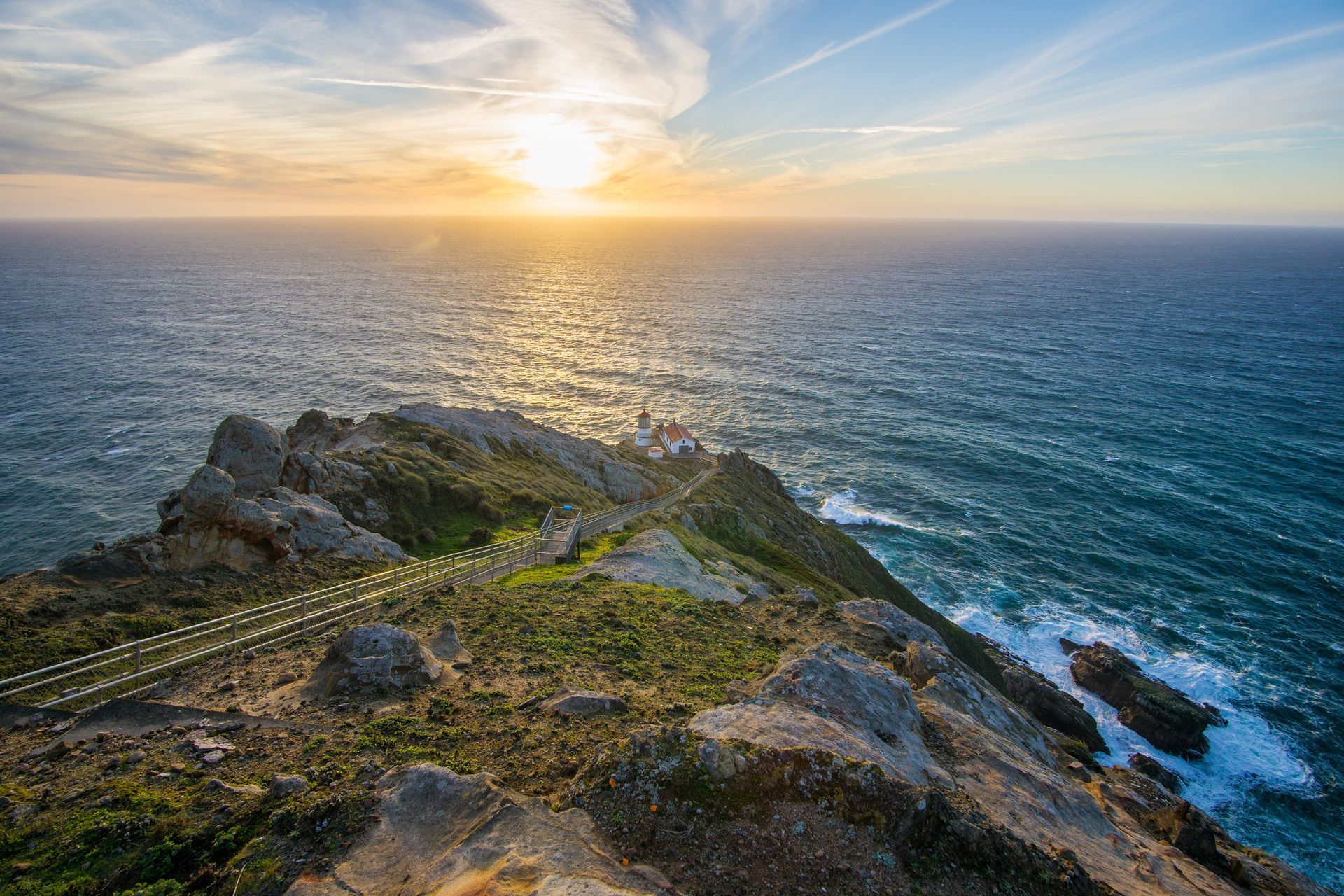 There is a lighthouse on the cliff overlooking the ocean at sunset.