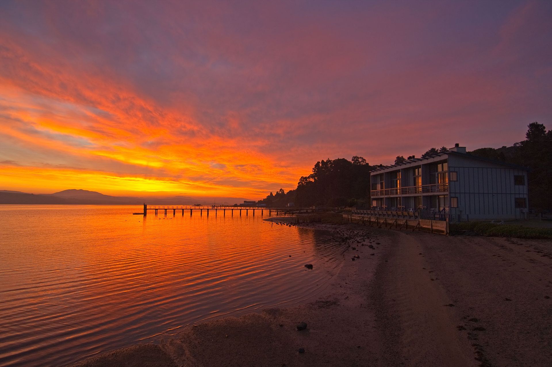 A sunset over a body of water with a dock in the foreground and a building in the background.