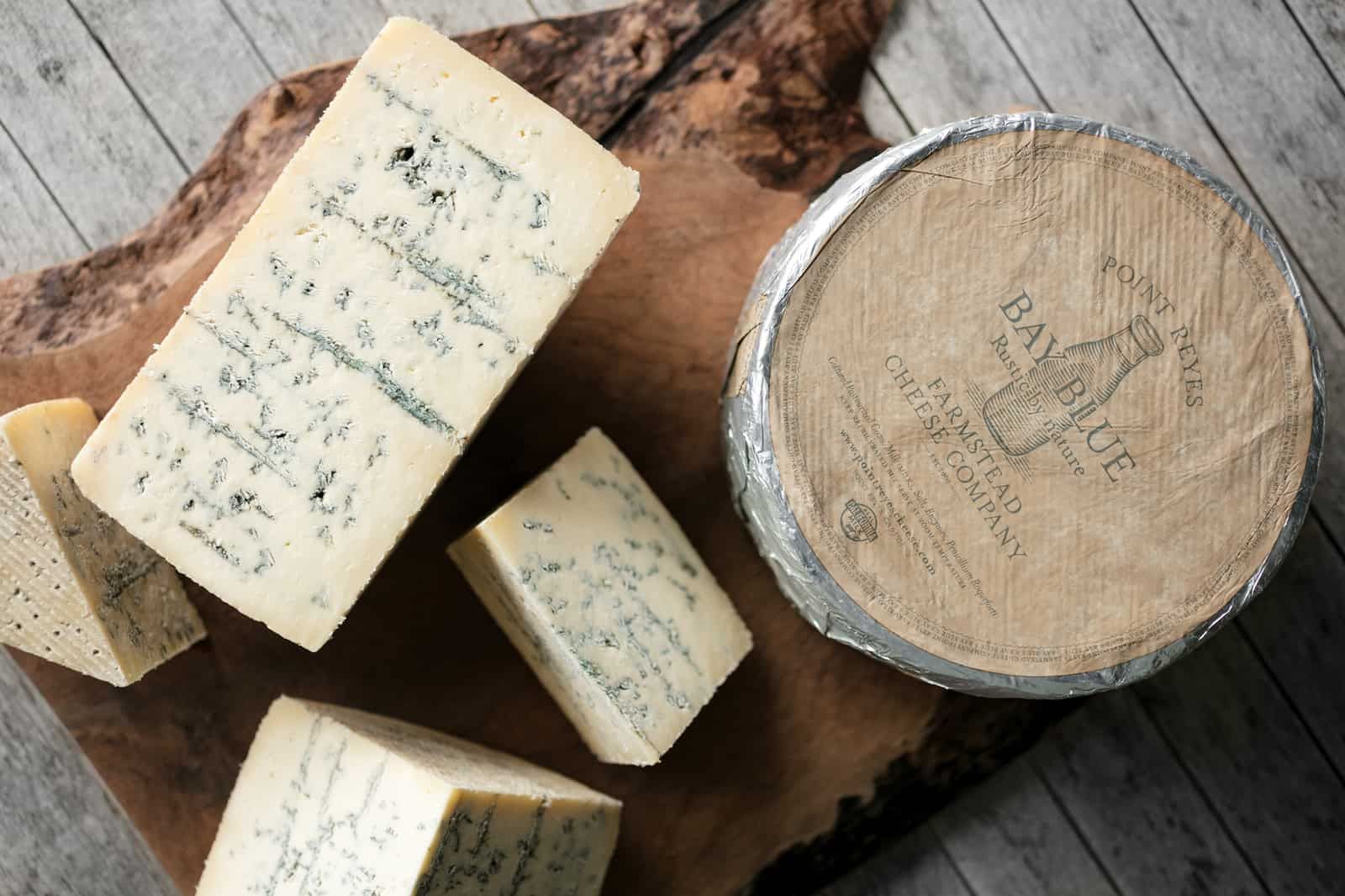 A wooden cutting board topped with pieces of cheese and a barrel of cheese.