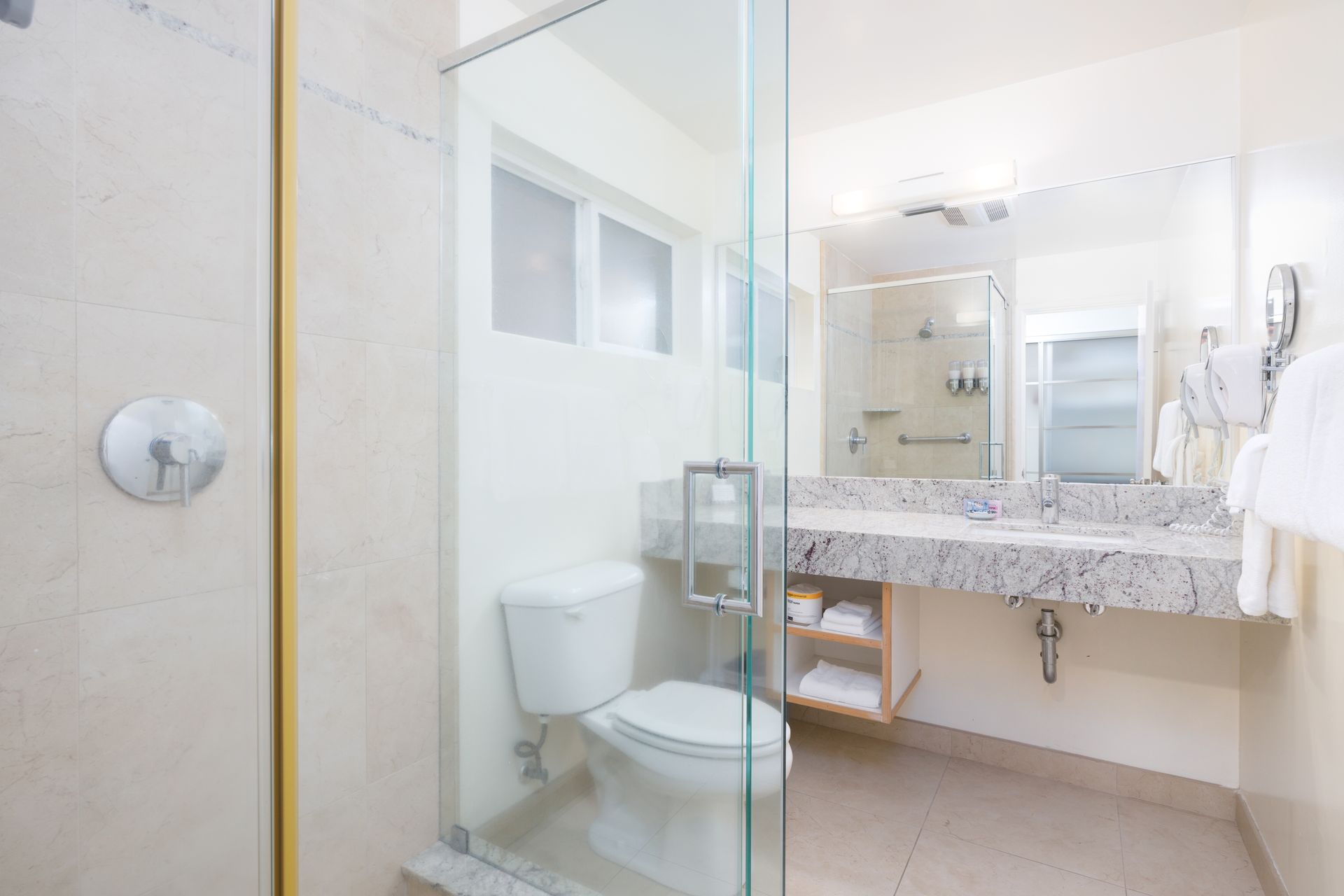 A bathroom in a hotel room with a toilet , sink and shower.