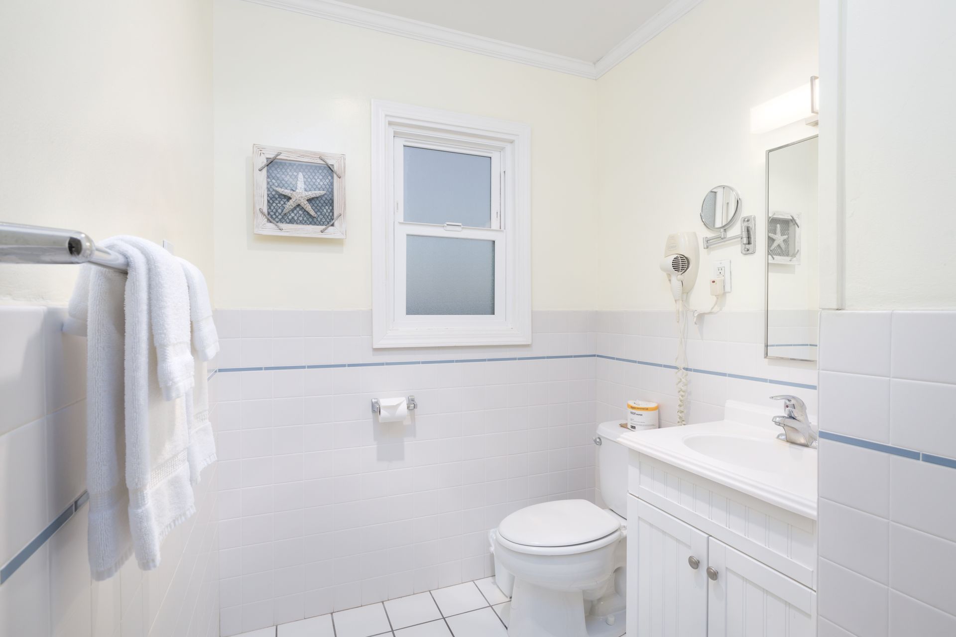 A bathroom with a toilet , sink , mirror and window.