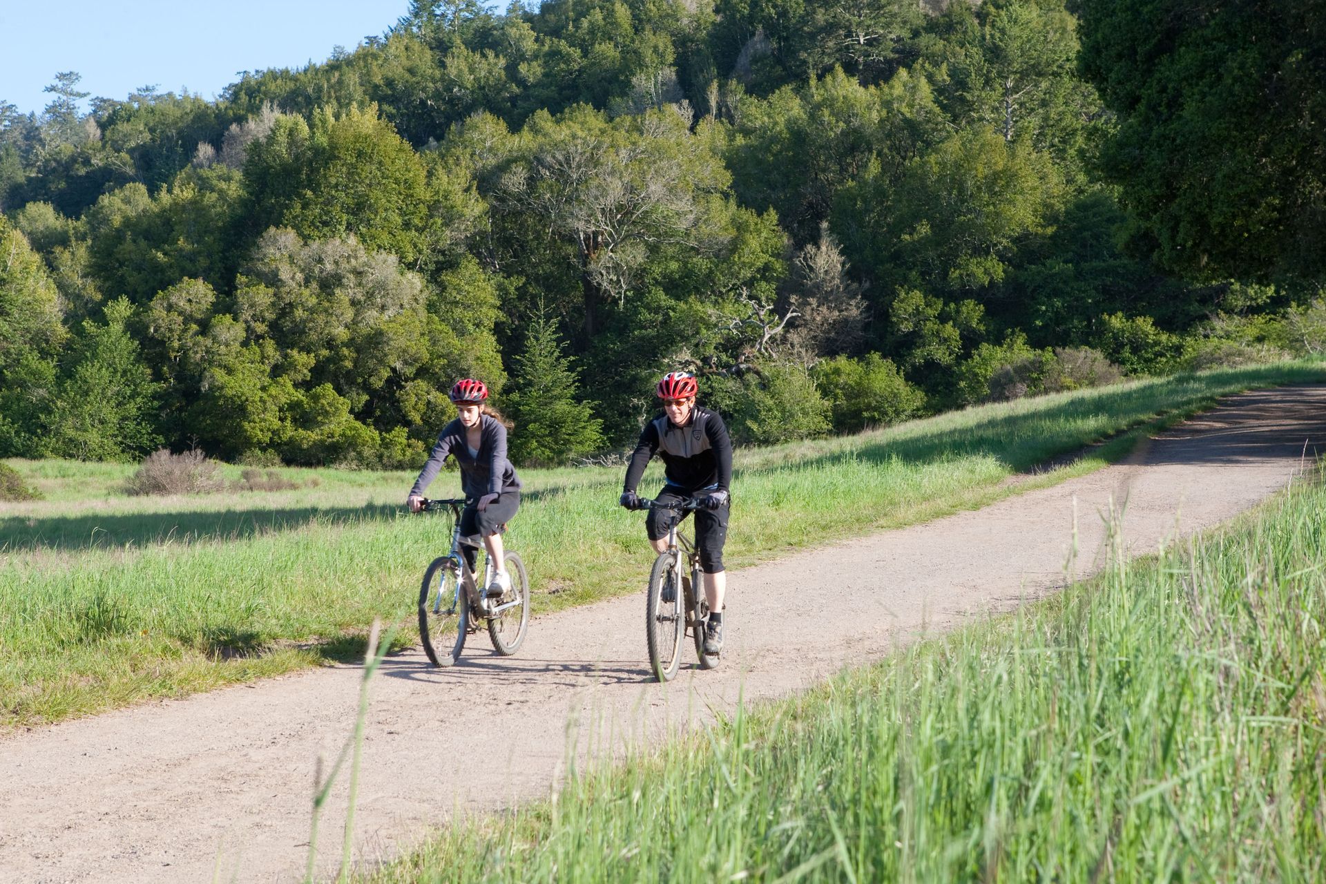 Two people are riding bikes down a dirt road.