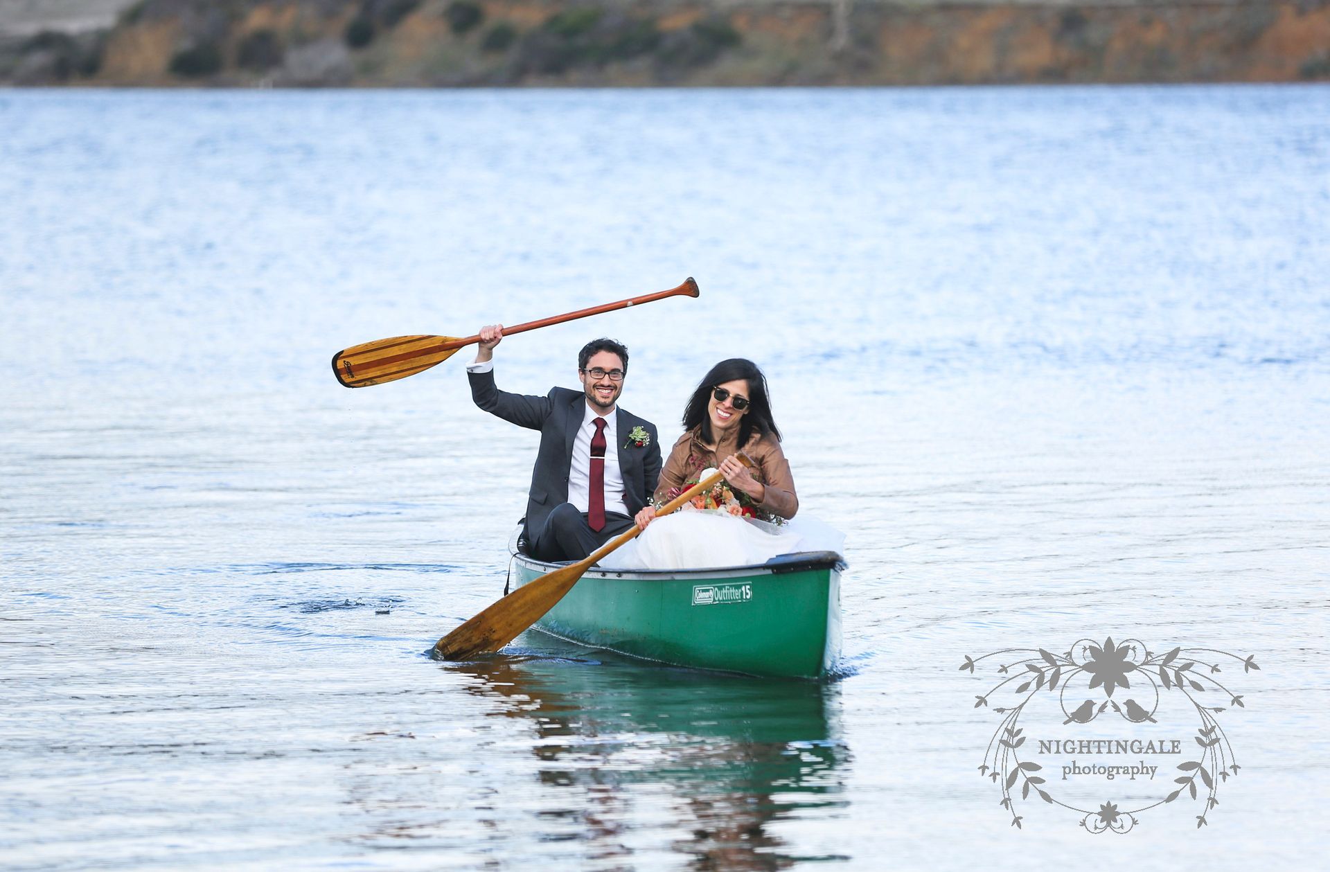 A bride and groom are rowing a canoe on a lake.