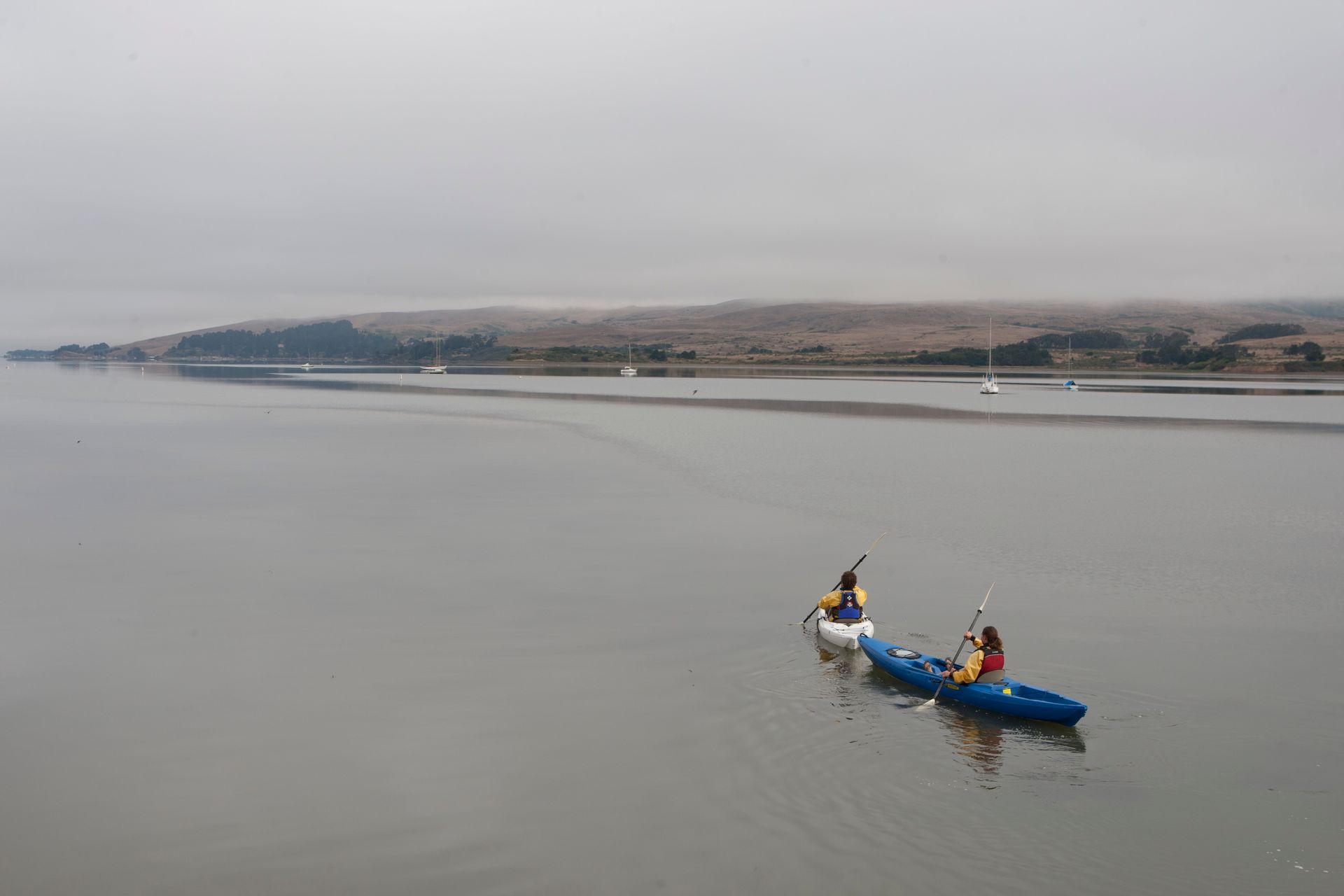 Two people are paddling kayaks on a lake