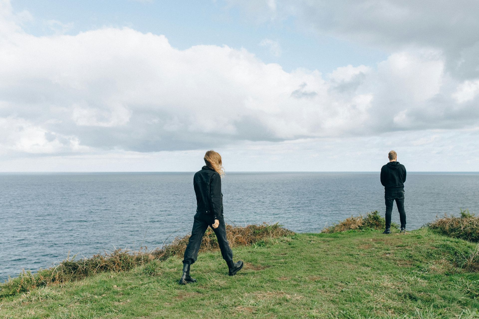 Two men are standing on a cliff overlooking the ocean.