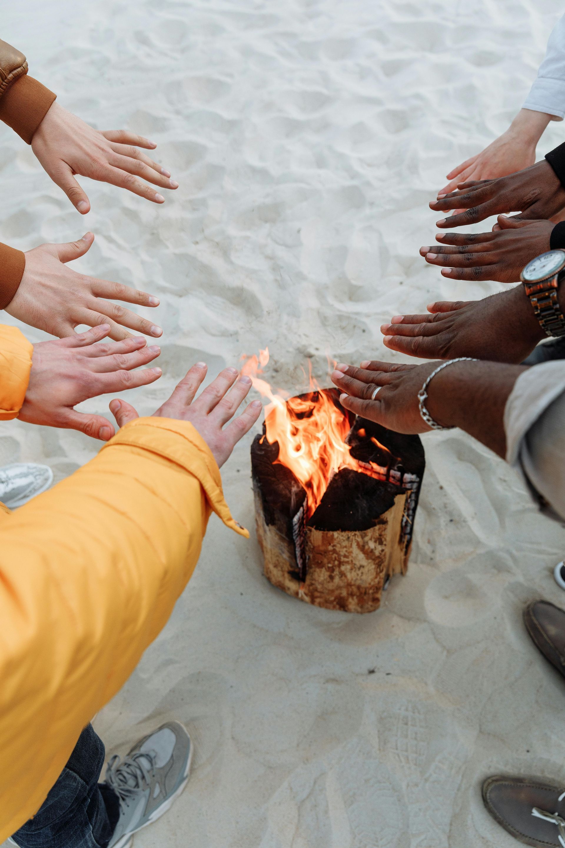 A group of people are warming their hands around a fire on the beach.