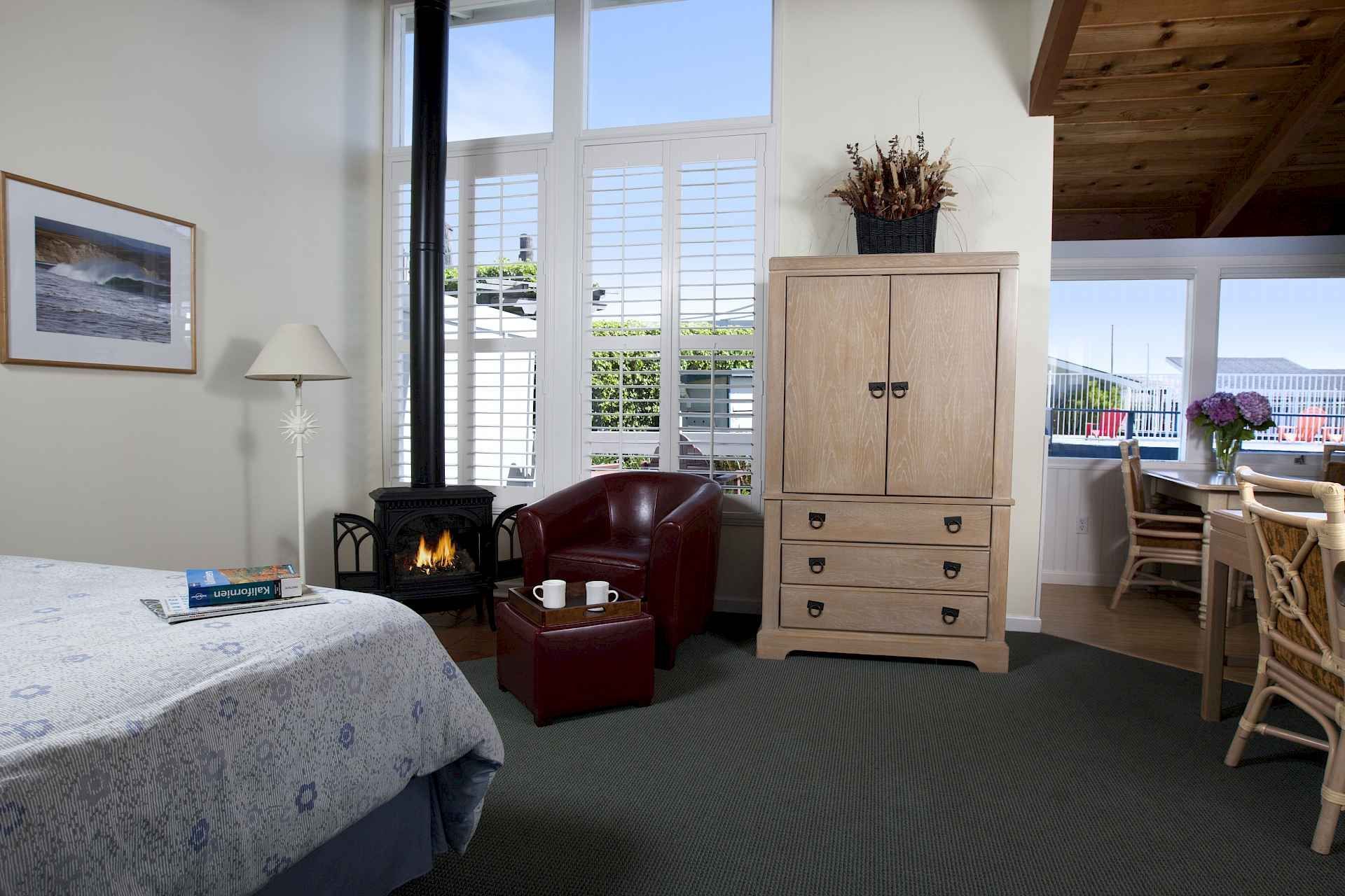 A bedroom with a bed a chair a dresser and a fireplace