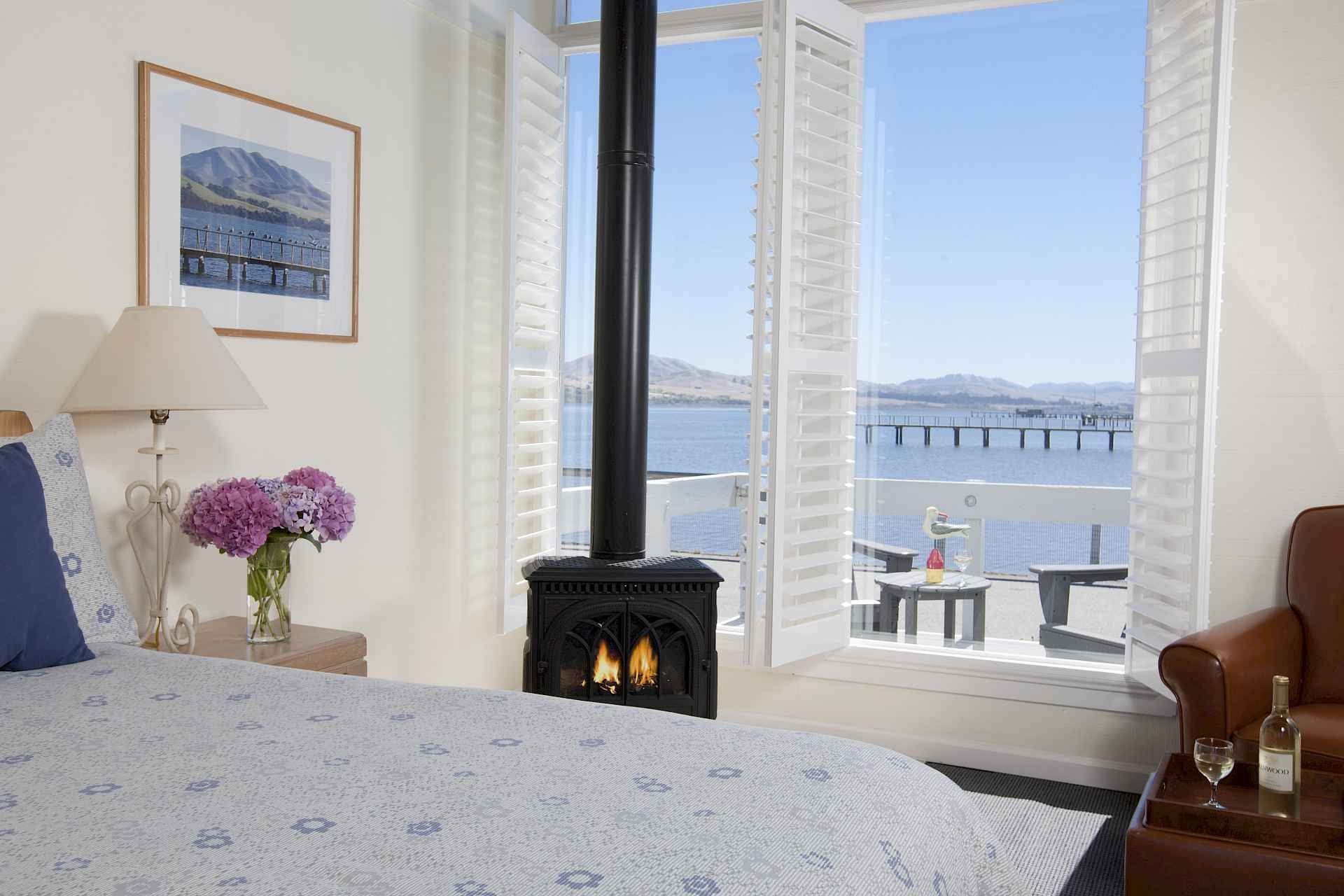 Bedroom with fireplace, bed, and open doors to a balcony overlooking the water.