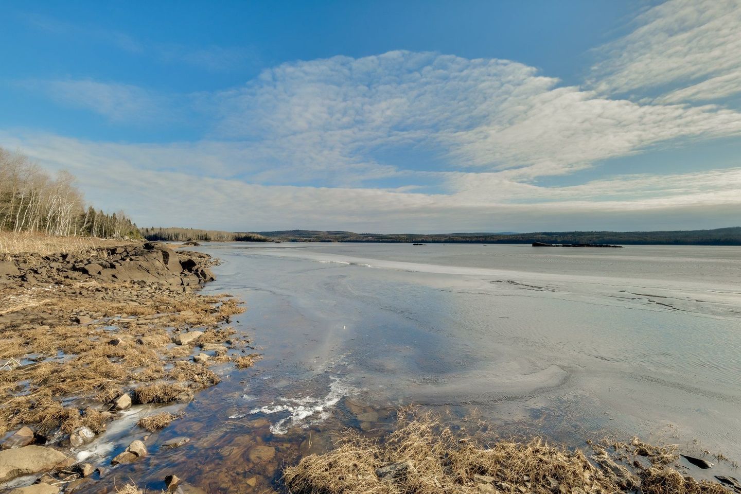 Un grand plan d'eau entouré de rochers et de glace par une journée ensoleillée.