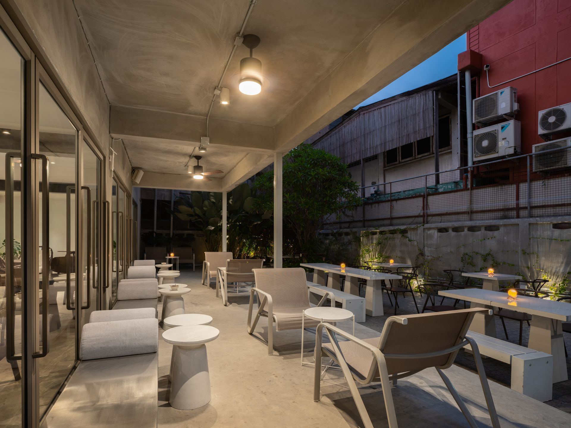 Outdoor patio seating with white tables and lounge chairs under a covered terrace at dusk